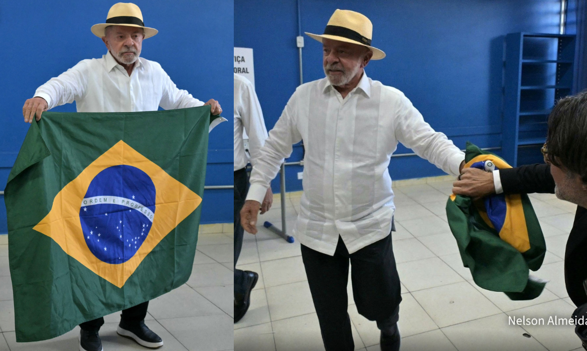 Imagem mostra o presidente Luiz In&aacute;cio Lula da Silva, candidato &agrave; reelei&ccedil;&atilde;o, entregando a bandeira a Ricardo Stuckert ap&oacute;s posar para fotos com a imprensa na se&ccedil;&atilde;o eleitoral.